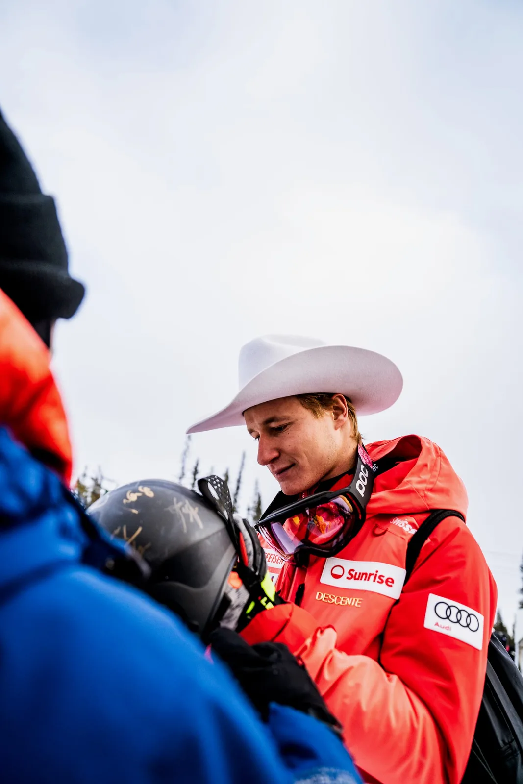 A Swiss ski racer in a white cowboy hat signing a fan's helmet at Lake Louise