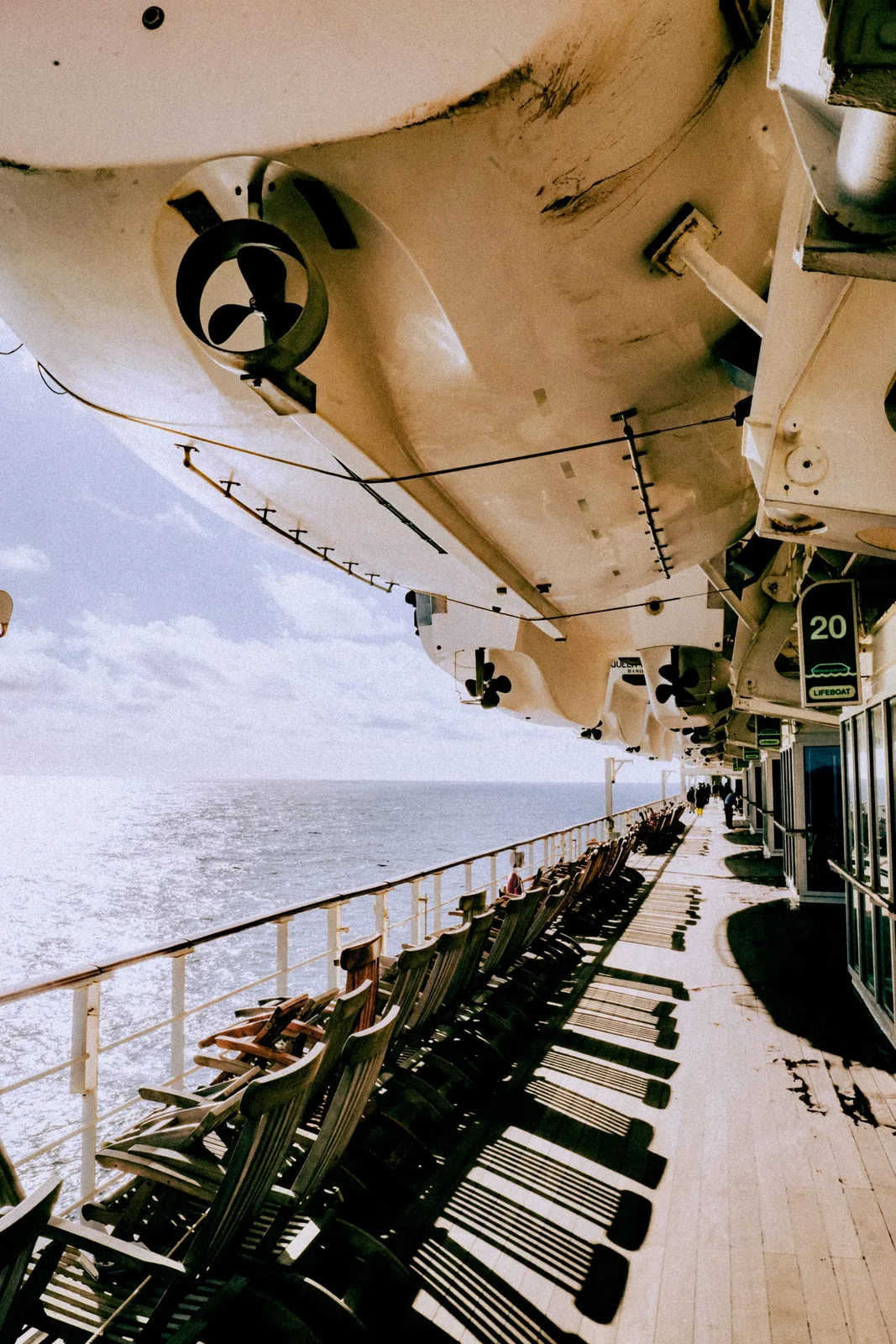 Wooden deck chairs lining the teak promenade beneath the lifeboats, the Atlantic stretching beyond the railing
