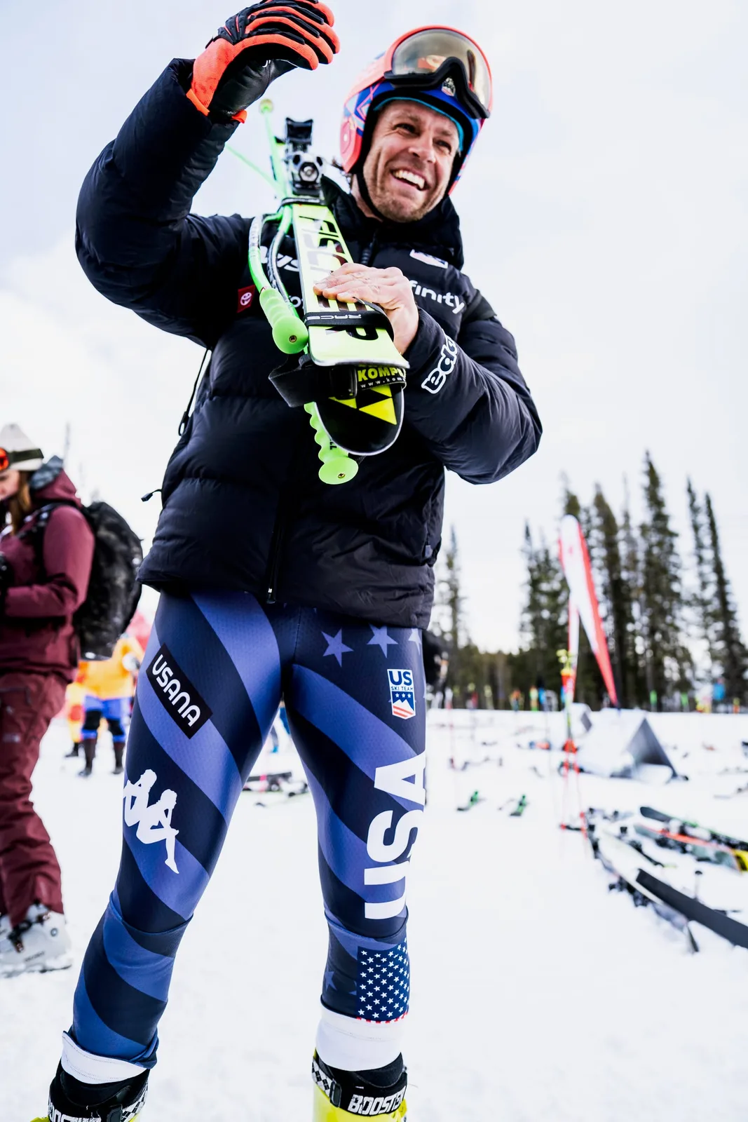 A US Ski Team racer laughing while carrying his skis in the Lake Louise finish area